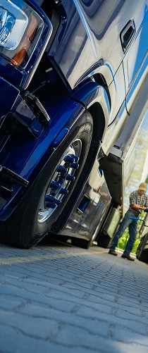Camion Poids Lourd Bleu: Entretien et Inspection Avant Départ Gros plan bas sur le pneu d'un camion semi-remorque bleu brillant. Un chauffeur fait l'entretien du poids lourd sur l'aire de stationnement.