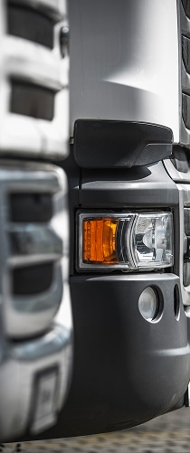 Phare de camion puissant : détail professionnel du pare-chocs. Détail avant d'un camion poids lourd: pare-chocs gris, phare intégré et clignotant orange. Design industriel et professionnel.