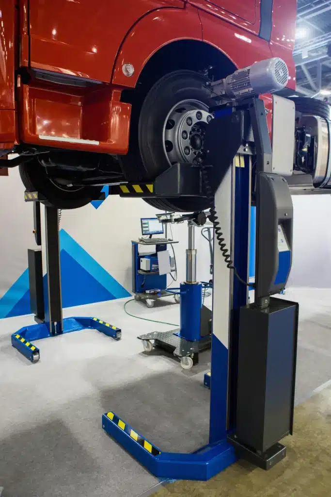 Pont Élévateur pour Camion : Maintenance Poids Lourds Camion rouge sur colonnes de levage mobiles bleues dans un atelier de maintenance pour poids lourds.